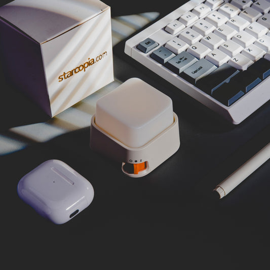 Small electronic device with orange accent on a dark surface next to a keyboard and box labeled 'starcopia.com'.