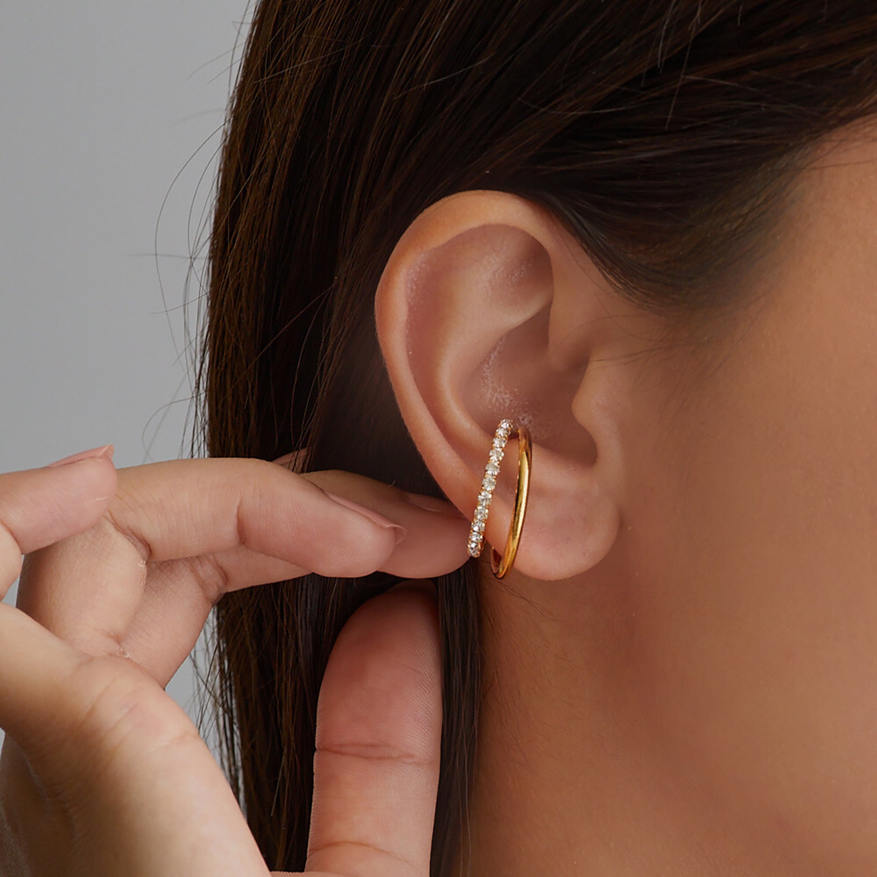 Gold hoop earring with clear gemstones worn by a person.