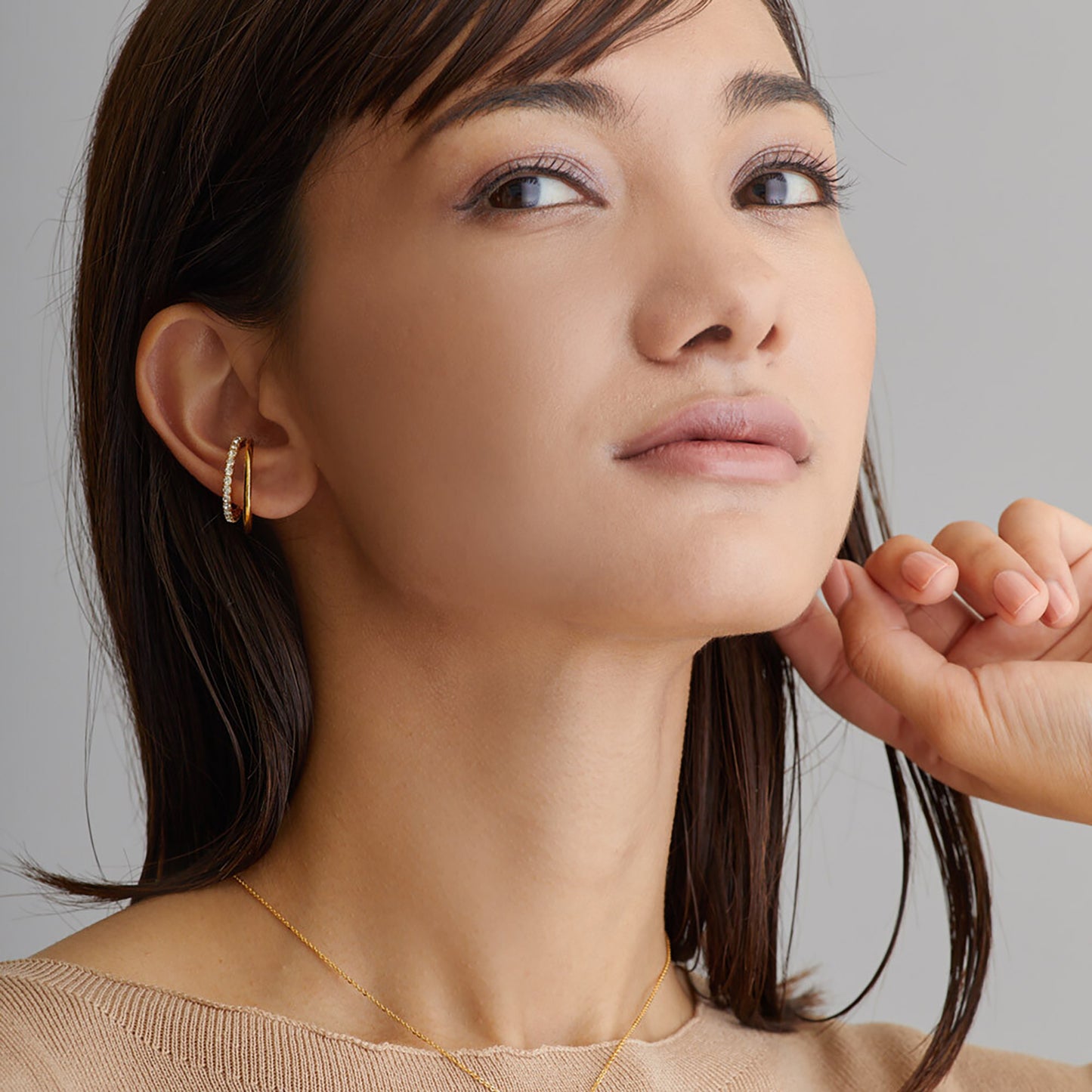 Close-up of a woman wearing gold earrings and a necklace against a neutral background