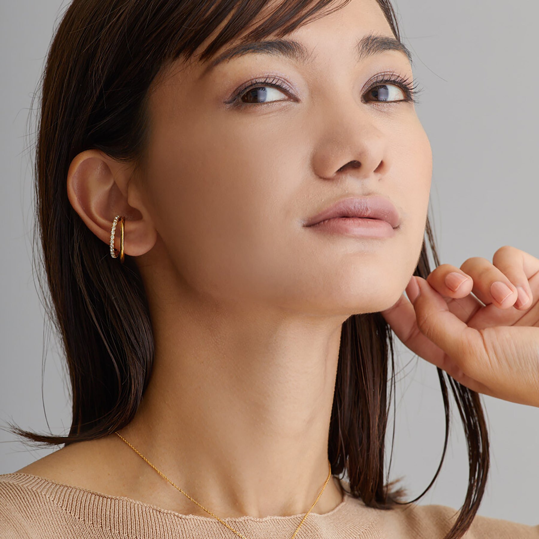 Close-up of a woman wearing gold earrings and a necklace against a neutral background