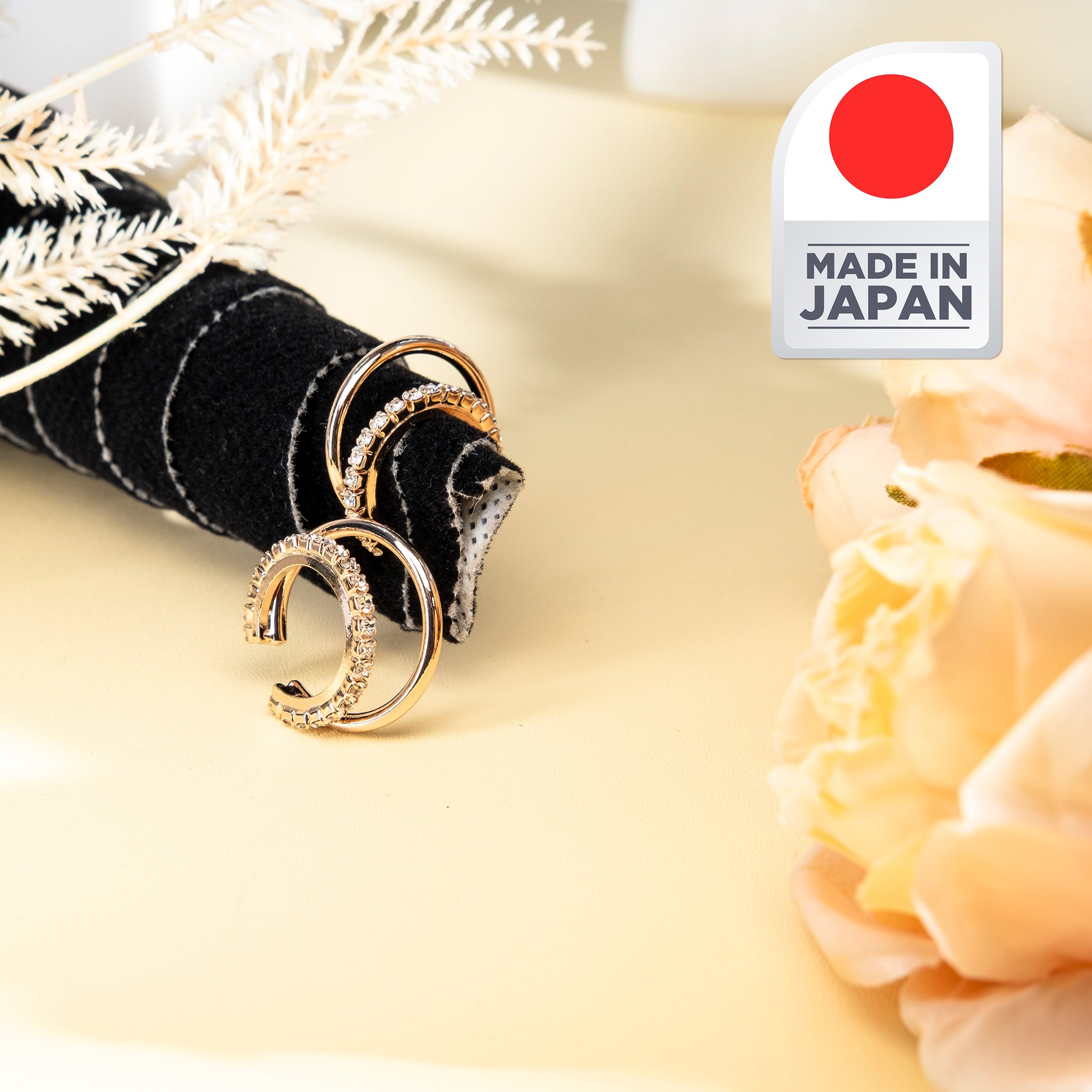 Gold earrings on a decorative stand with a 'Made in Japan' label and flowers in the background